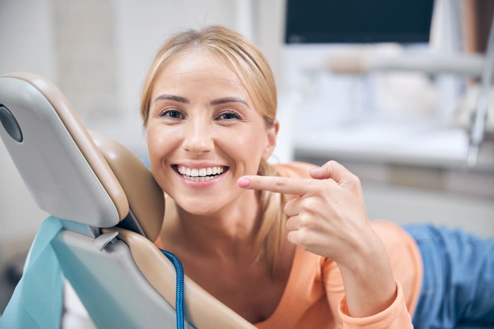 A smiling patient in the treatment chair pointing at her teeth