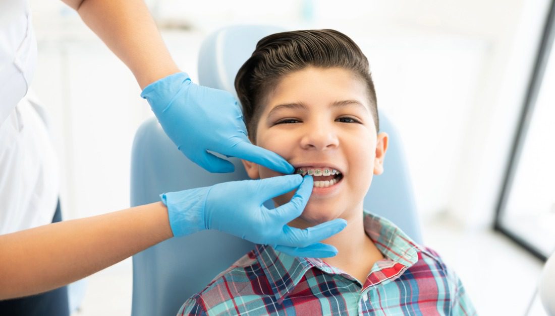 A young patient with braces smiling in the chair while a clinical team member checks his brackets