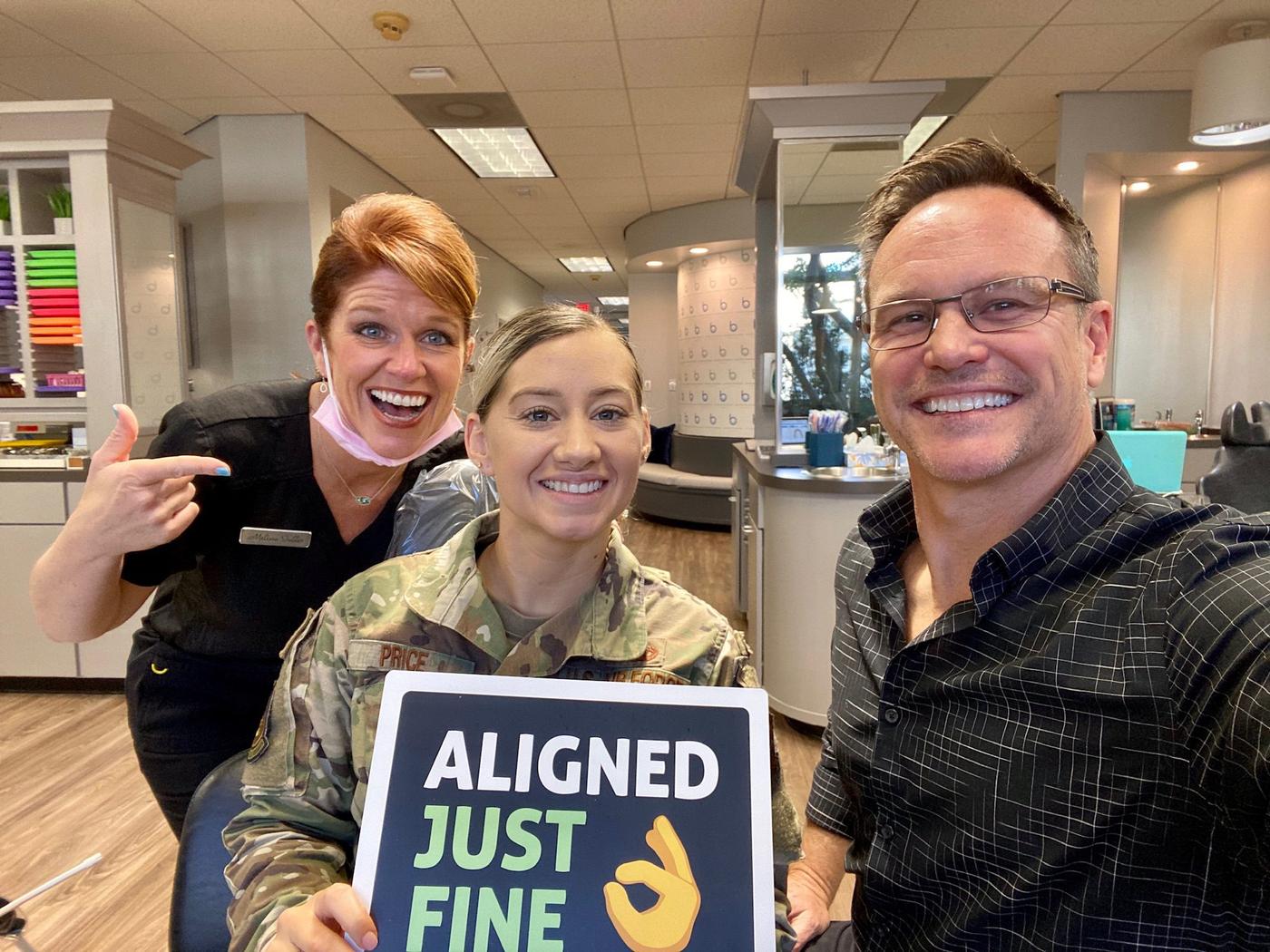 Dr. Bowman and team member Melissa at Brodie Bowman Orthodontics with an Air Force service member holding an Aligned Just Fine sign