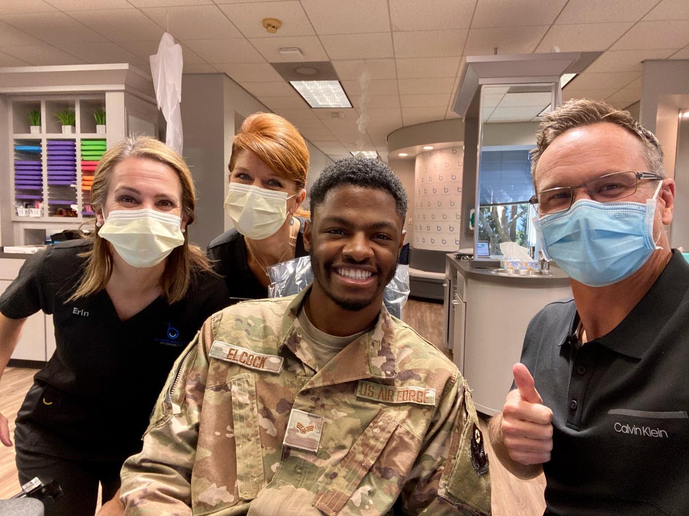A smiling Air Force patient with Erin, the team, and Dr. Bowman giving a thumbs-up at Brodie Bowman Orthodontics